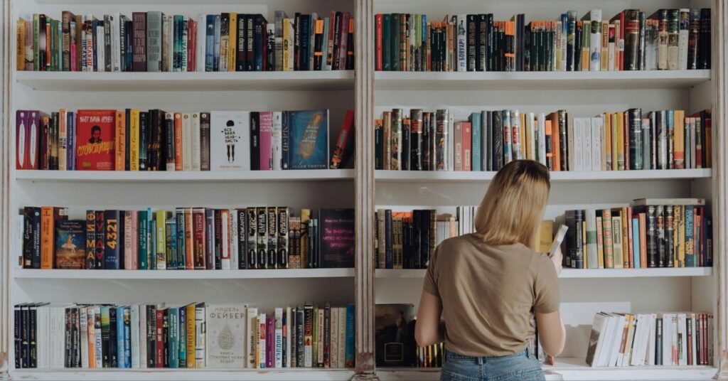 A person browsing colorful books on a white bookshelf, representing design inspiration and creative learning.